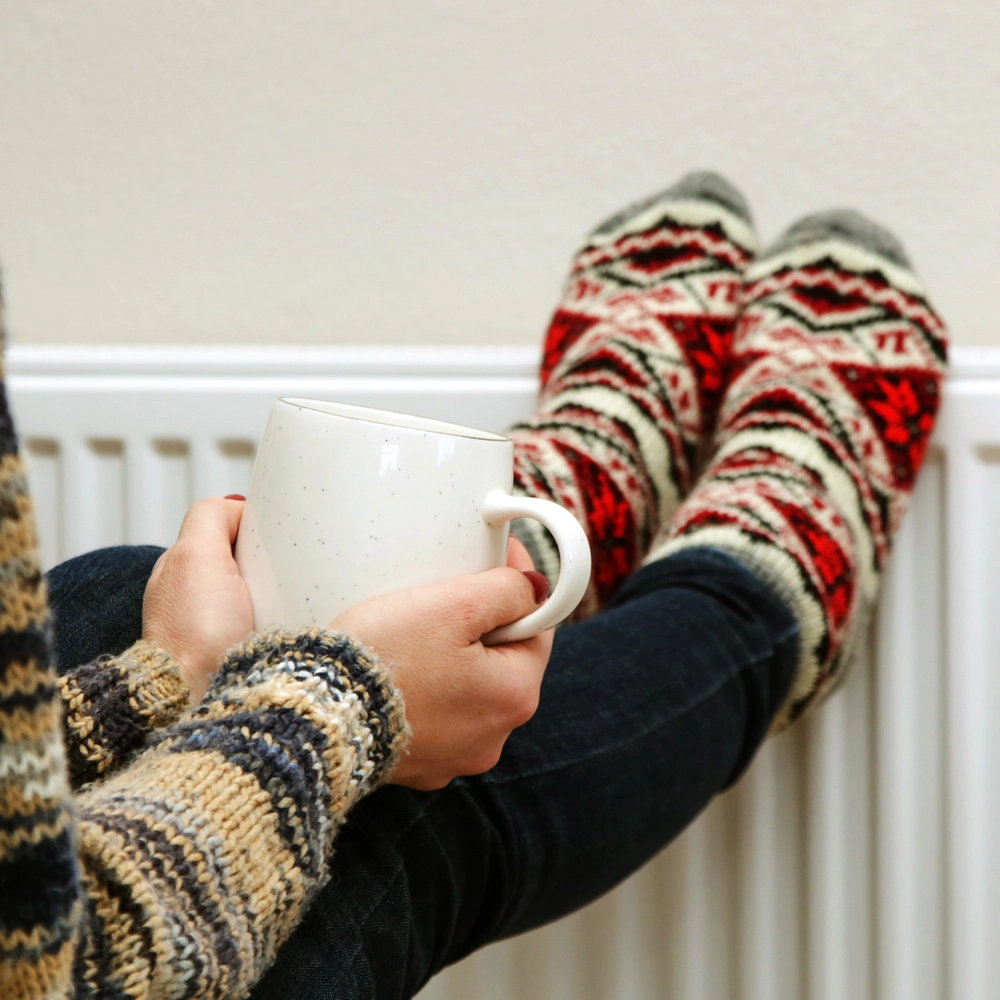 Kvinde med striktrøje, kaffekop og striksokker, der hviler på radiator