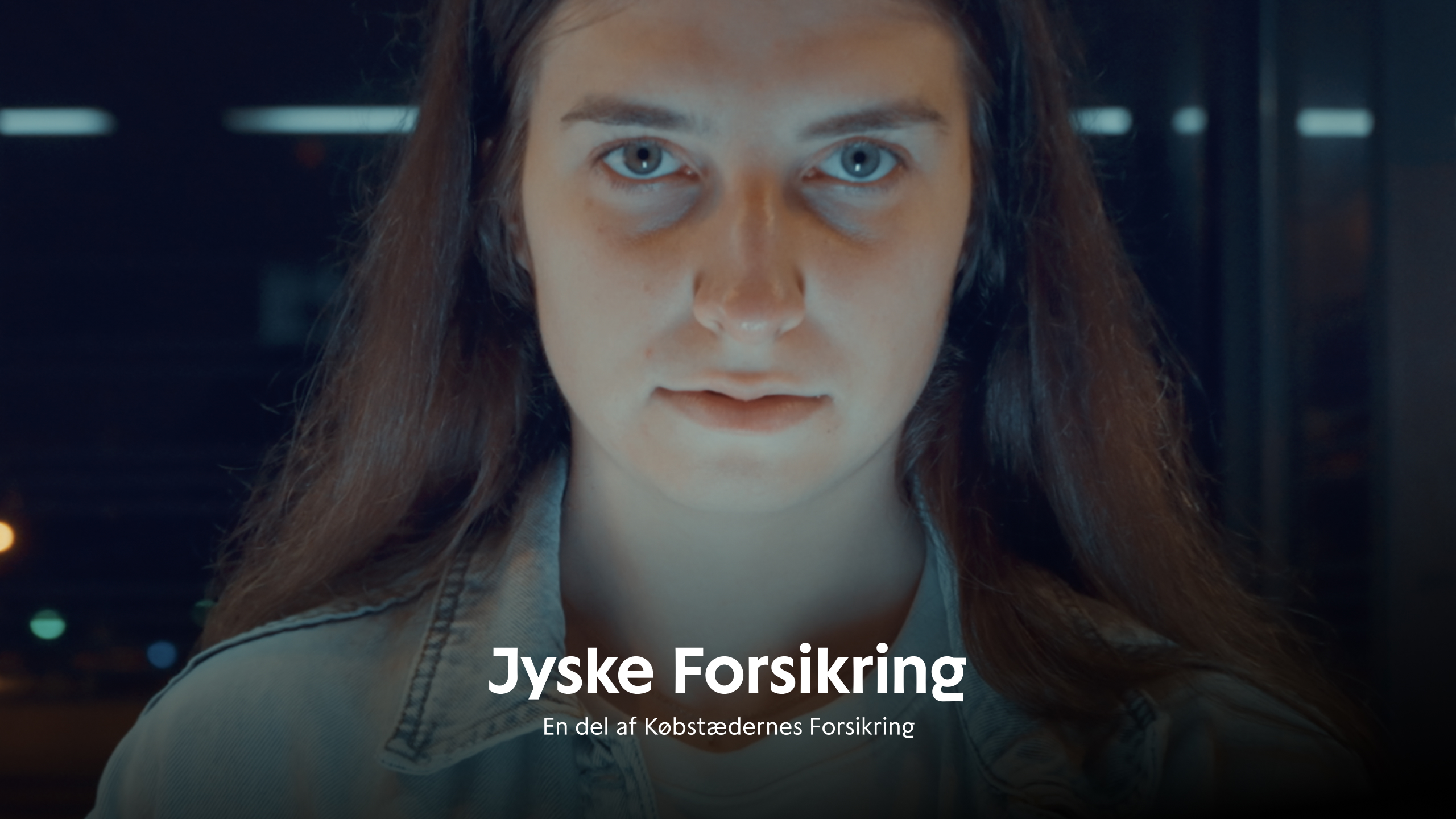 Ung kvinde i mørkt rum med tekst "Jyske Forsikring // En del af Købstædernes Forsikring"