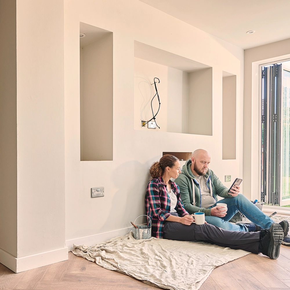 Mand og kvinde sidder op af væg i hus under renovering