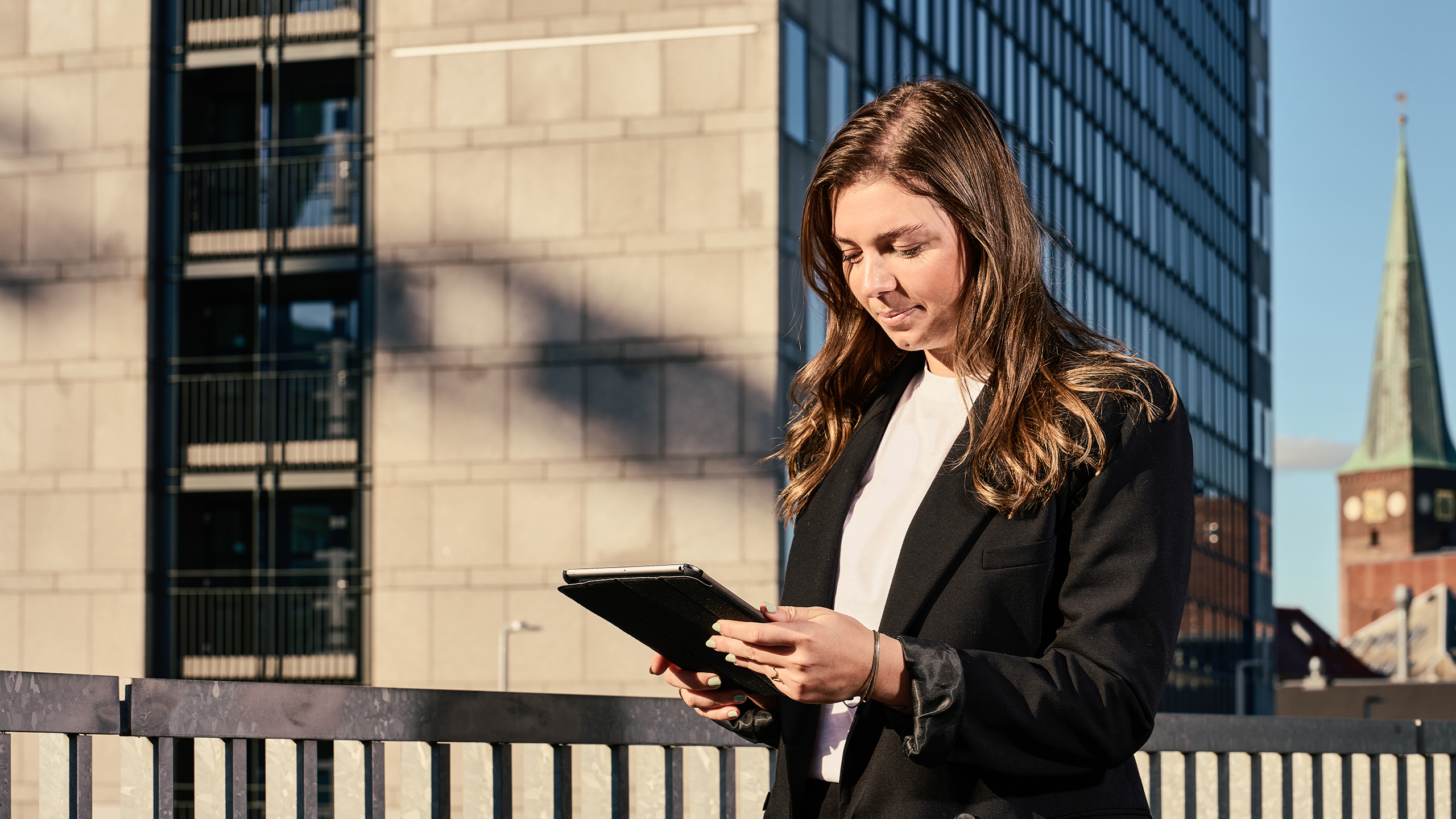 Kvinde kigger på iPad foran moderne bygning