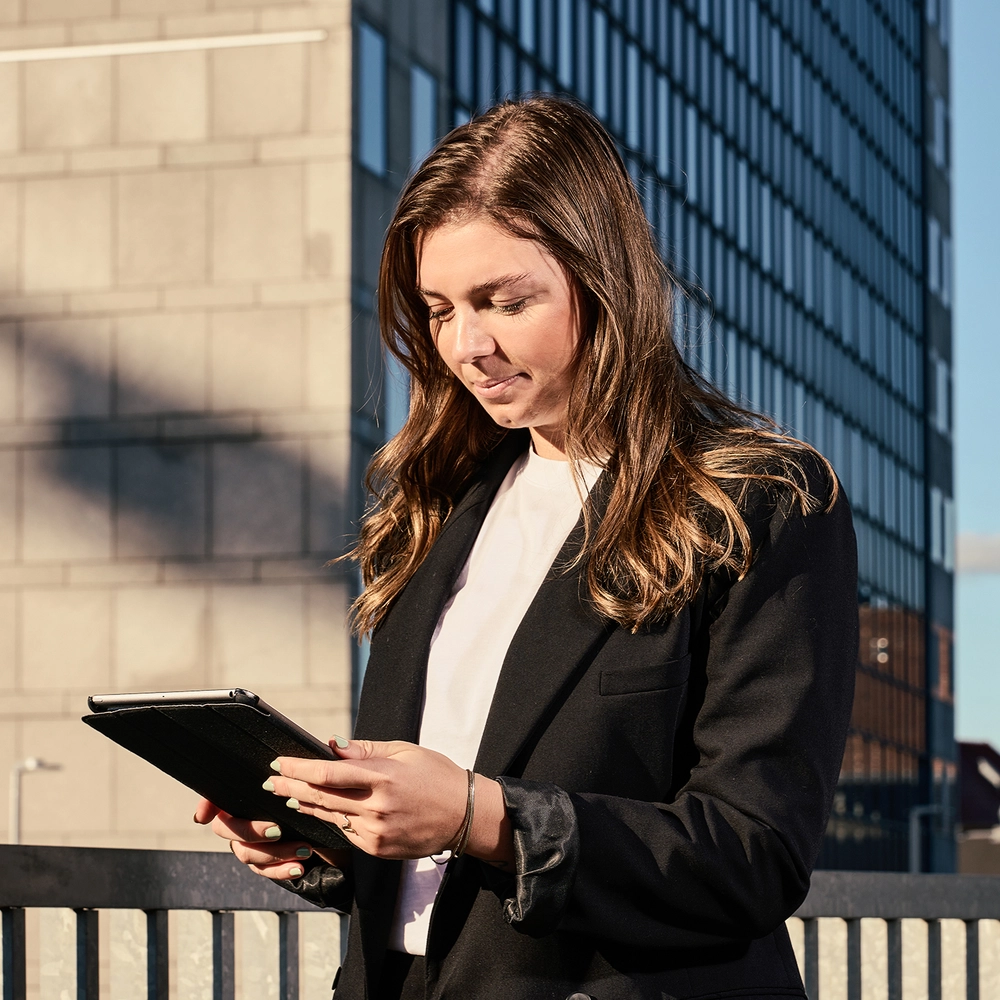 Kvinde kigger på iPad foran moderne bygning