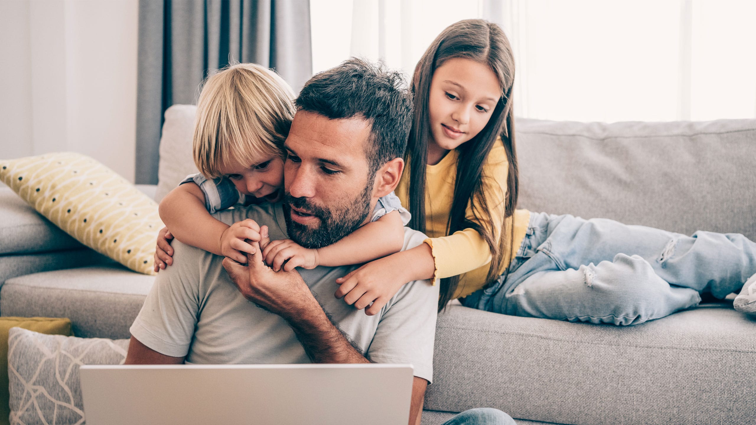 To børn i sofa og far på gulvet med computer