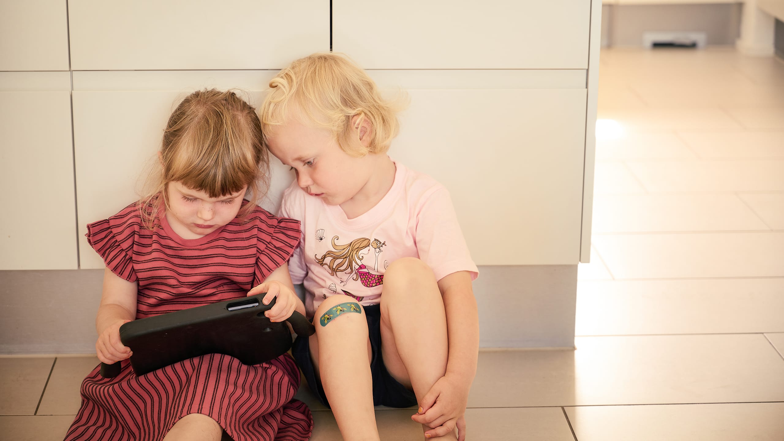 To piger sidder på gulv med tablet