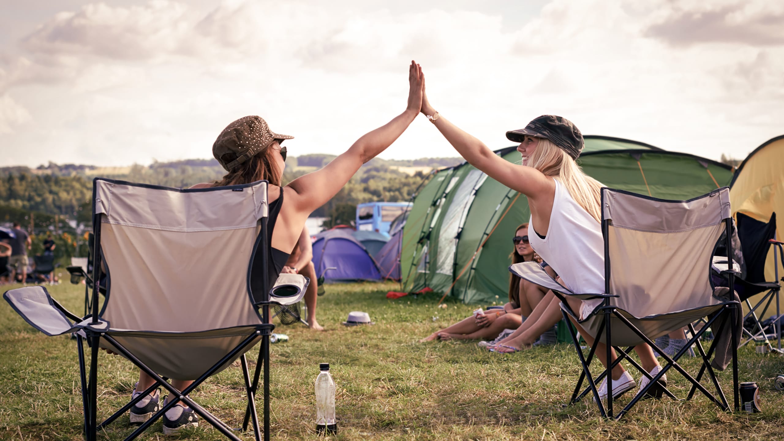 Festivaldeltagere giver en highfive til hinanden mens de sidder i deres lejr