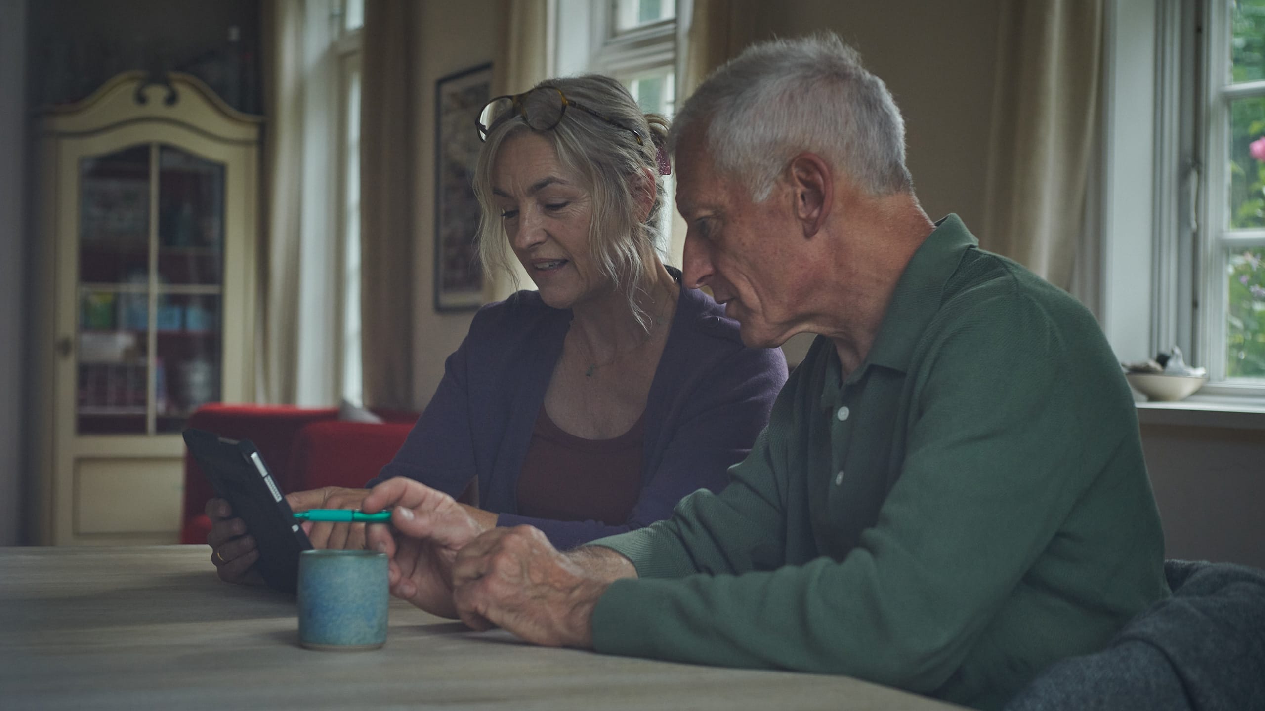 To mennesker sidder ved middagsbordet og kigger på en tablet sammen. De sidder i et pænt hus.