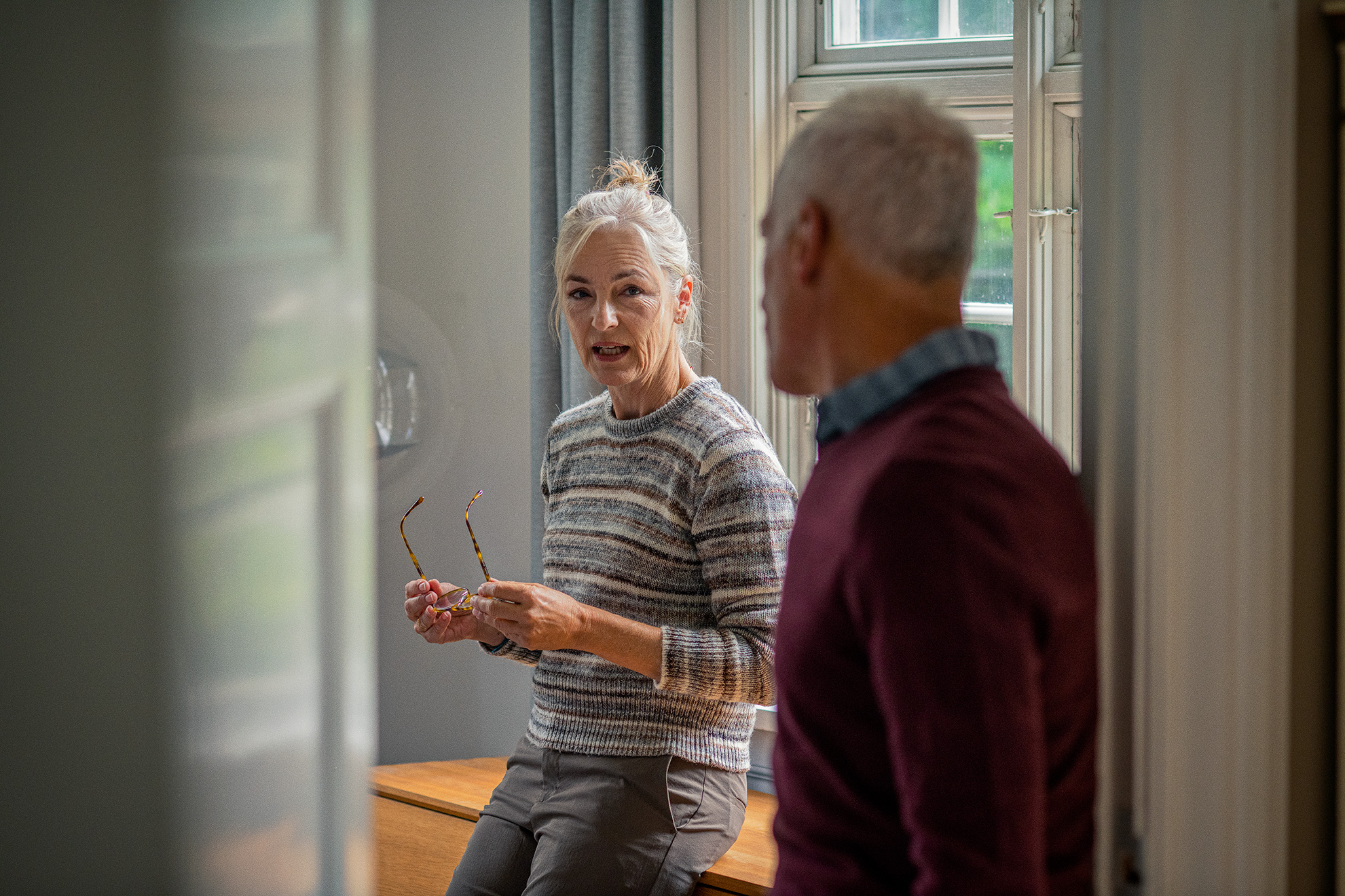 Ældre kvinde med briller sidder på en skænk og taler med en mand