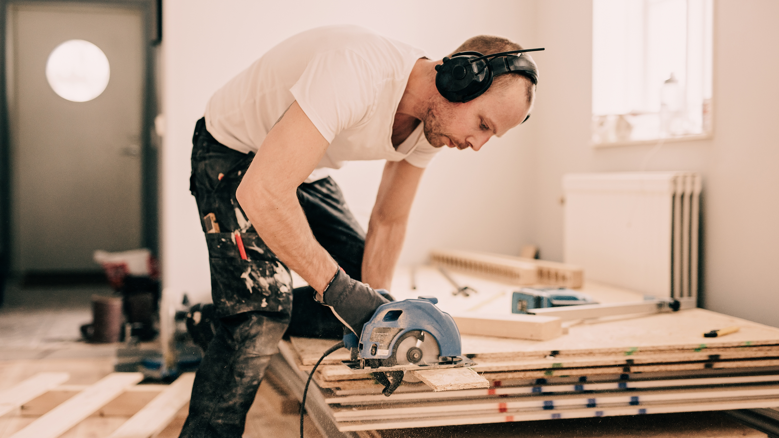 Tømrer med høreværn og rundsav arbejder på byggeprojekt