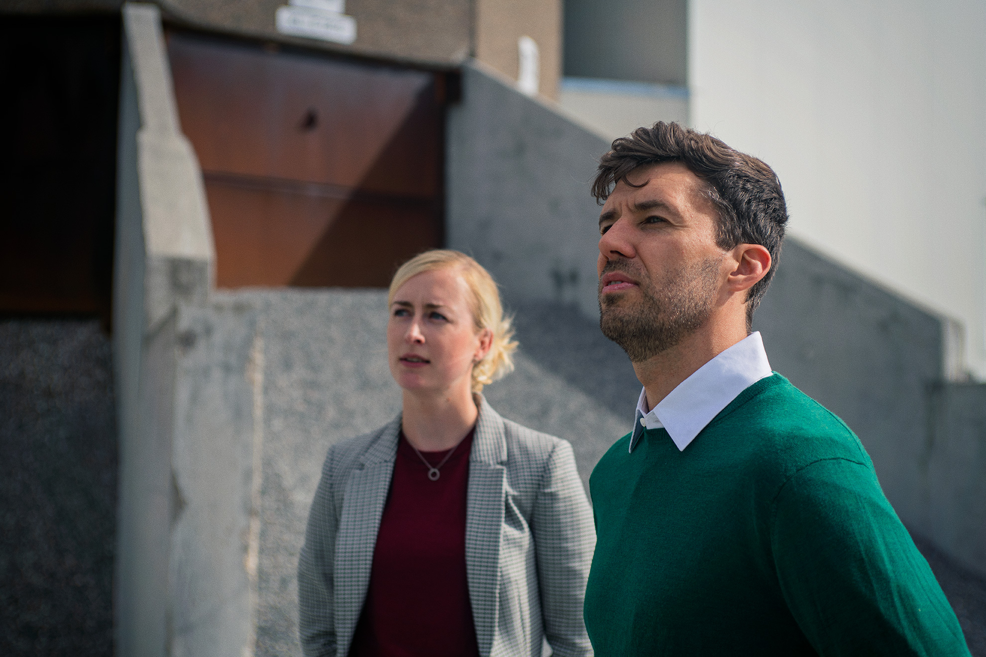 Mand i skjorte og grøn pullover med kvinde i rød trøje og gråternet blazer