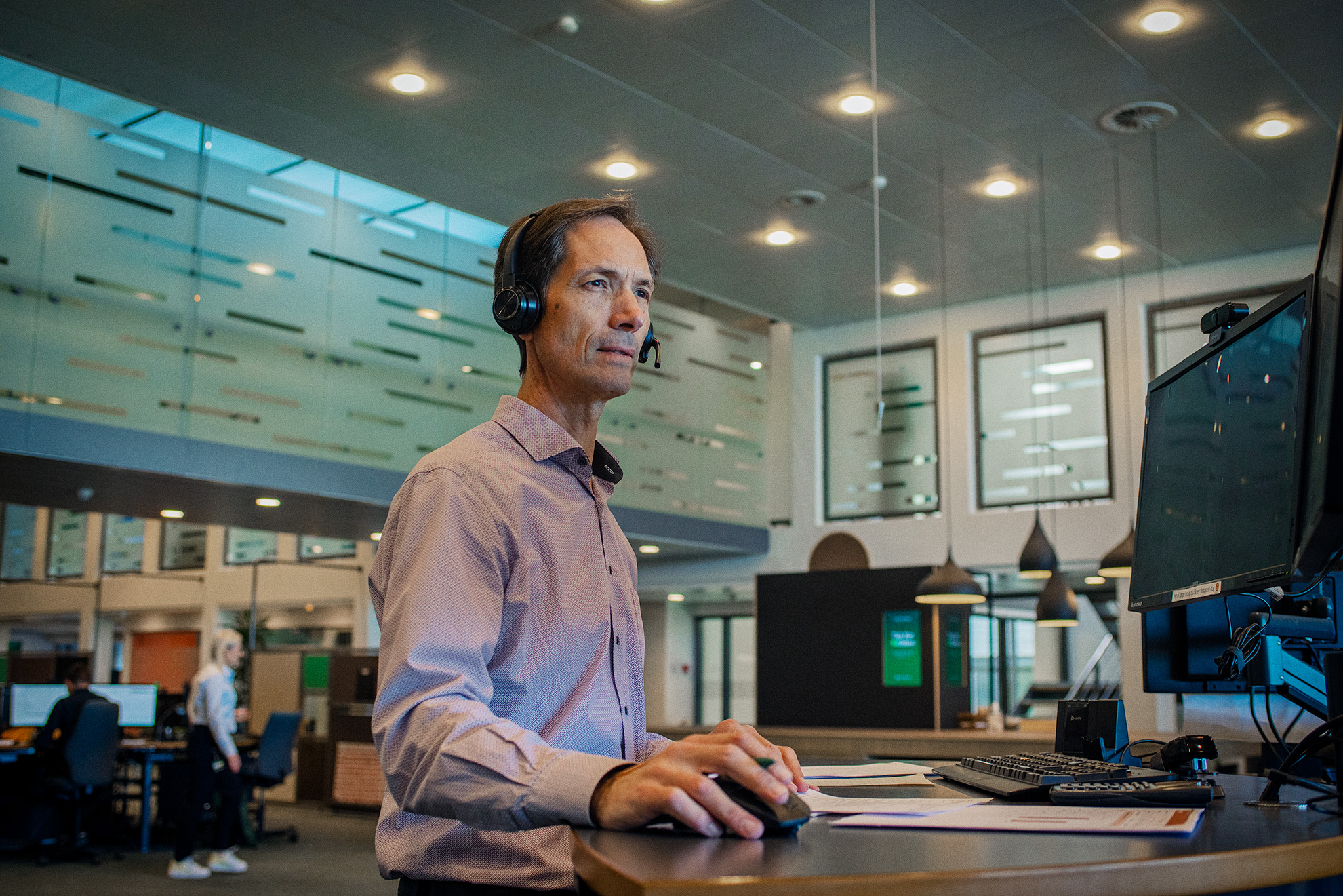 Mand med headset foran computer i moderne storkontor