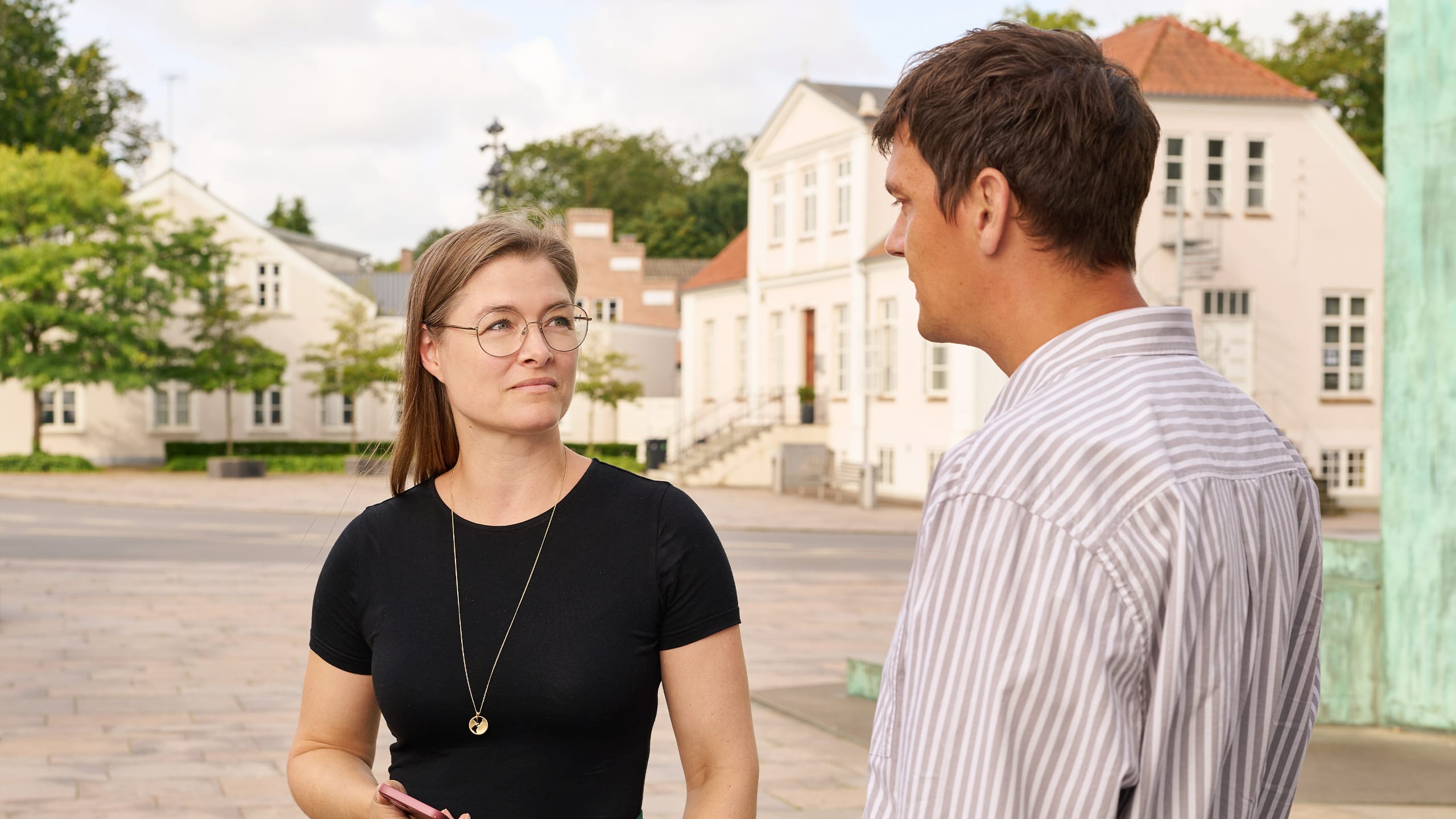 Kvinde og mand i dialog foran bygning