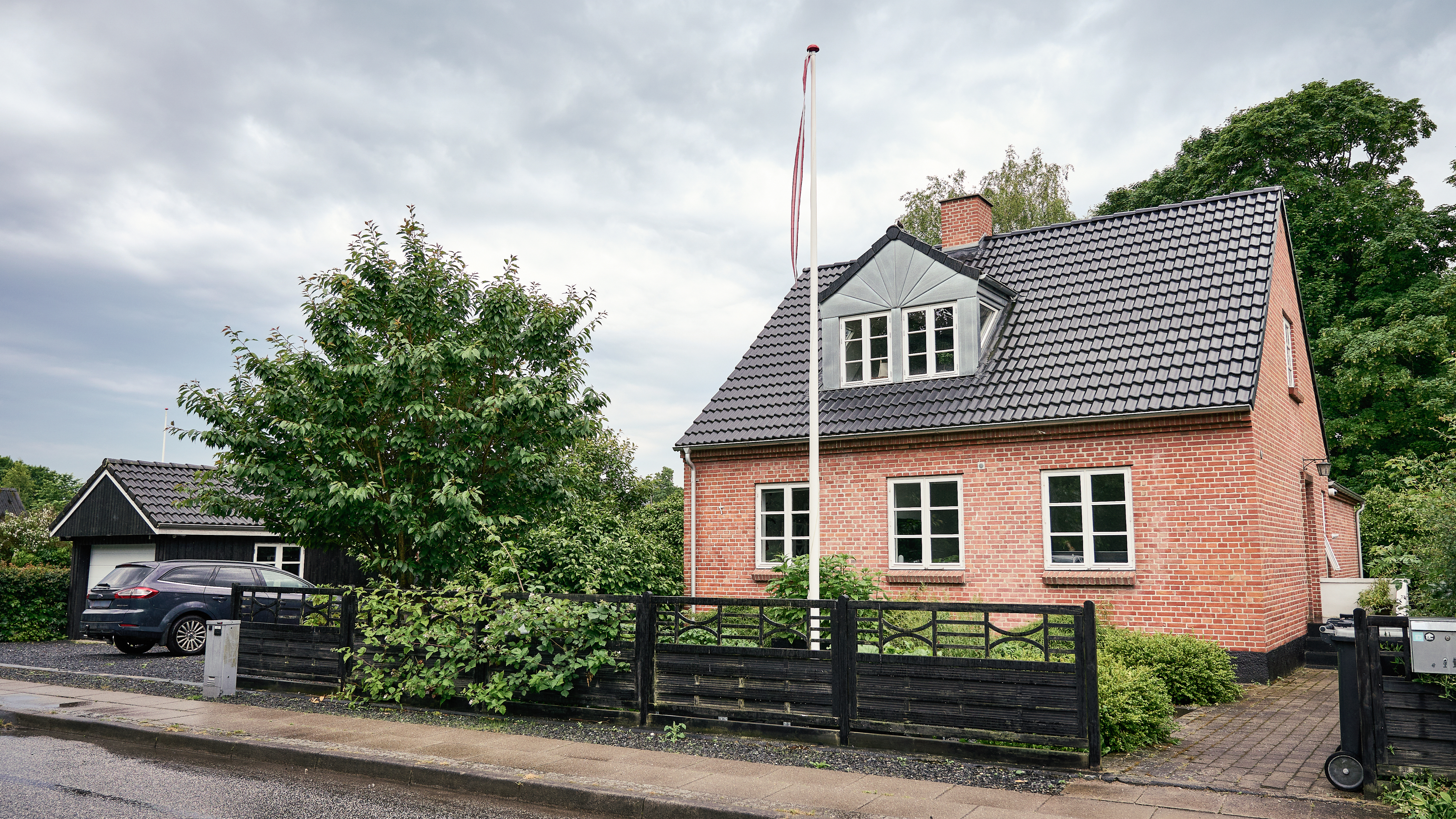 Rødt murstenshus med flagstang og familiebil foran