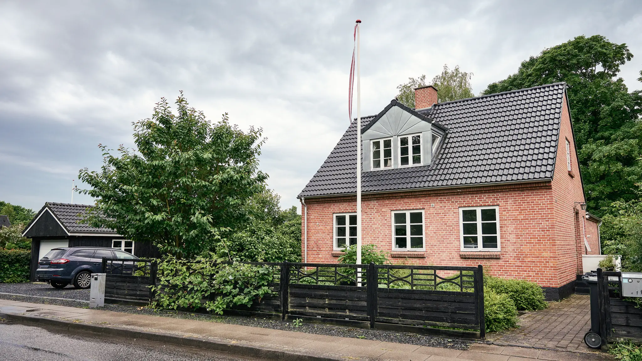 Rødt murstenshus med flagstang og familiebil foran