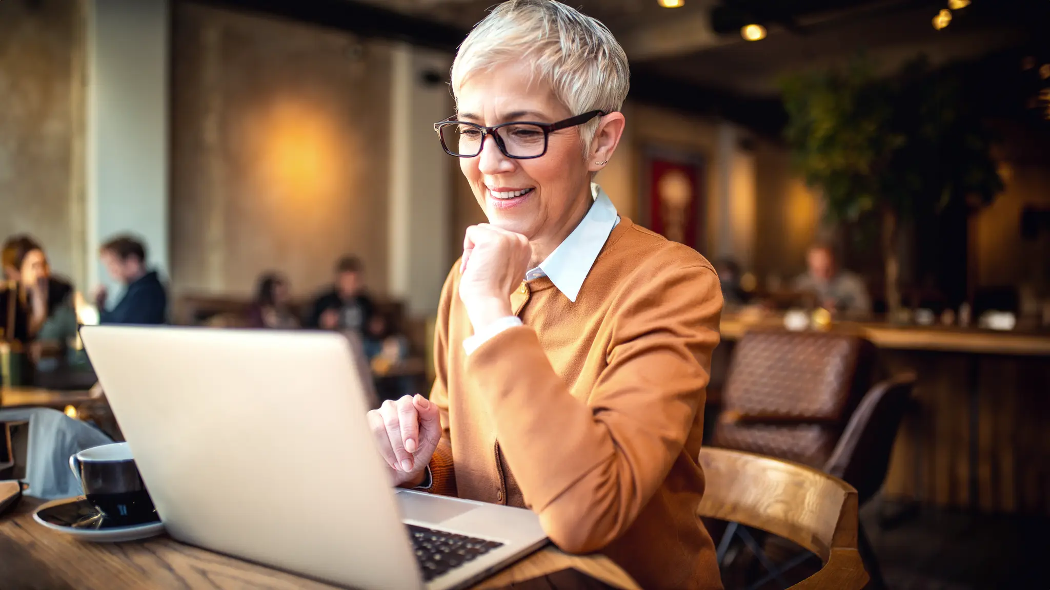 Smilende kvinde på café med laptop foran sig