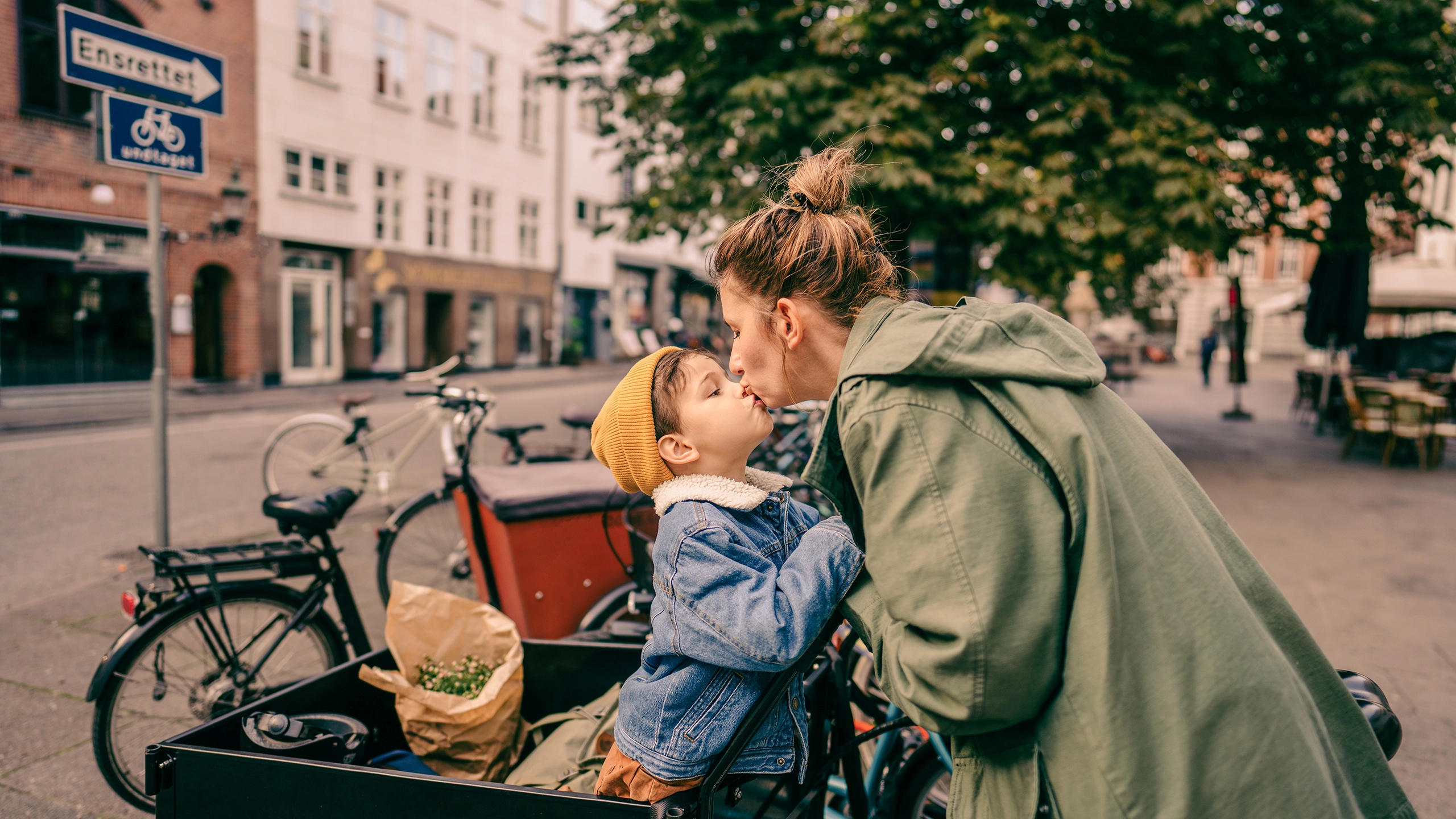 Kvinde kysser sit barn, som sidder i ladcykel