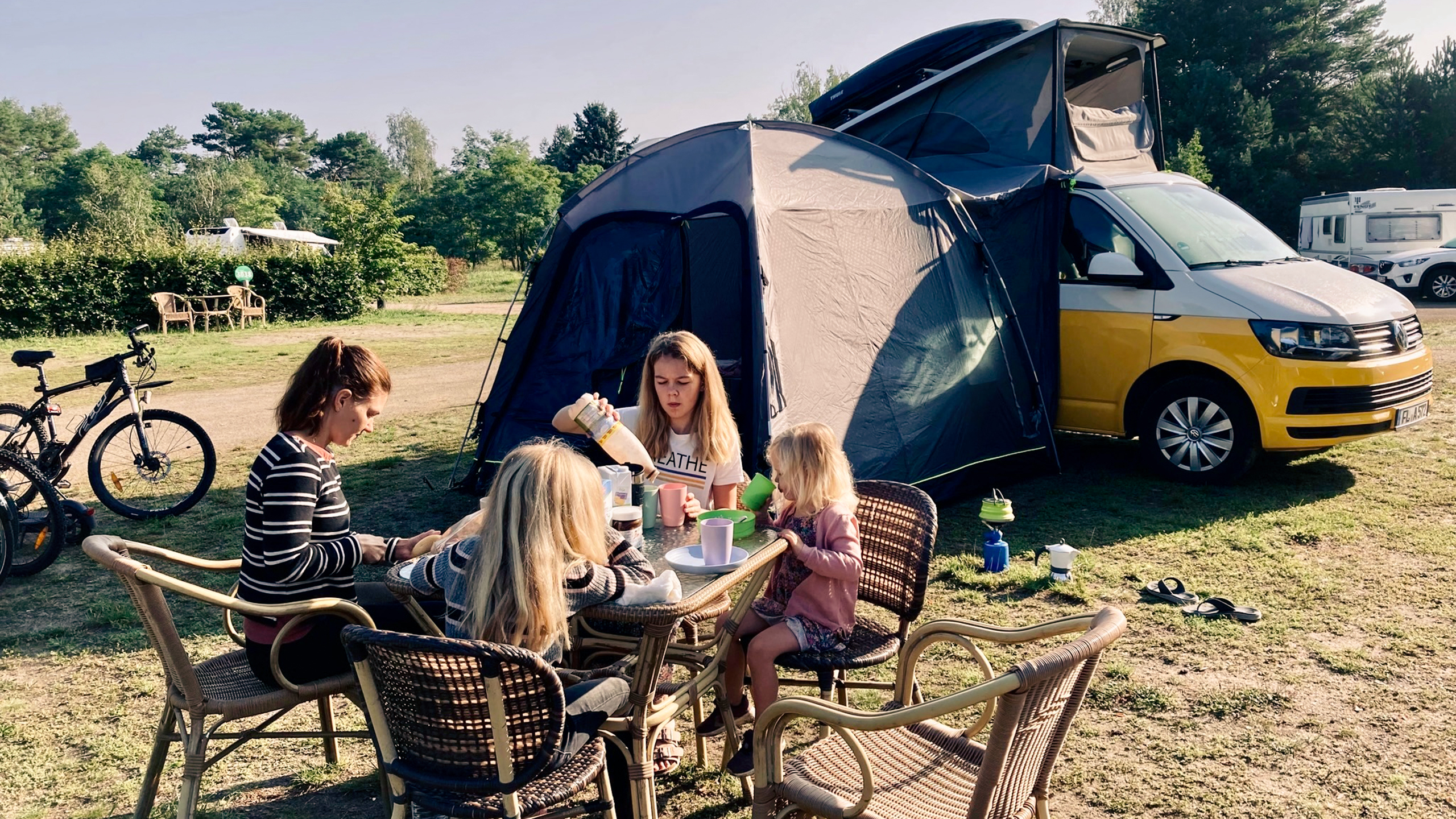 Kvinde og tre børn ved bord på campingplads